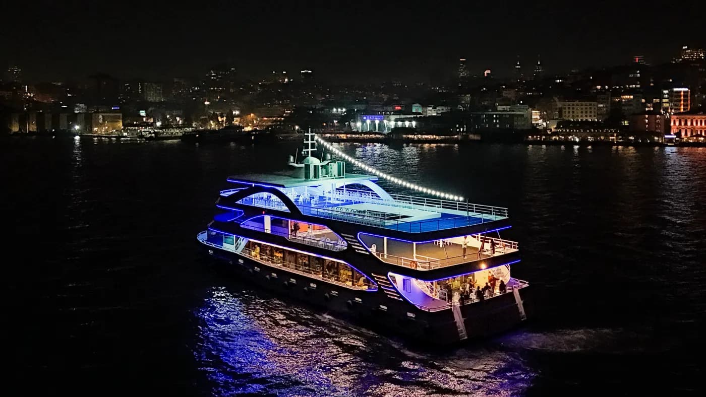 Barco Touronic Cruise navegando o Bósforo à noite com o horizonte de Istambul ao fundo